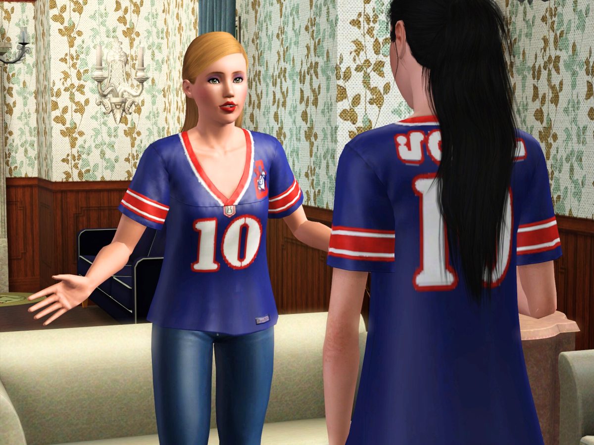 Two animated female characters wearing matching blue sports jerseys with the number 10 and red accents, standing in a living room with floral wallpaper. One character is gesturing while speaking to the other.