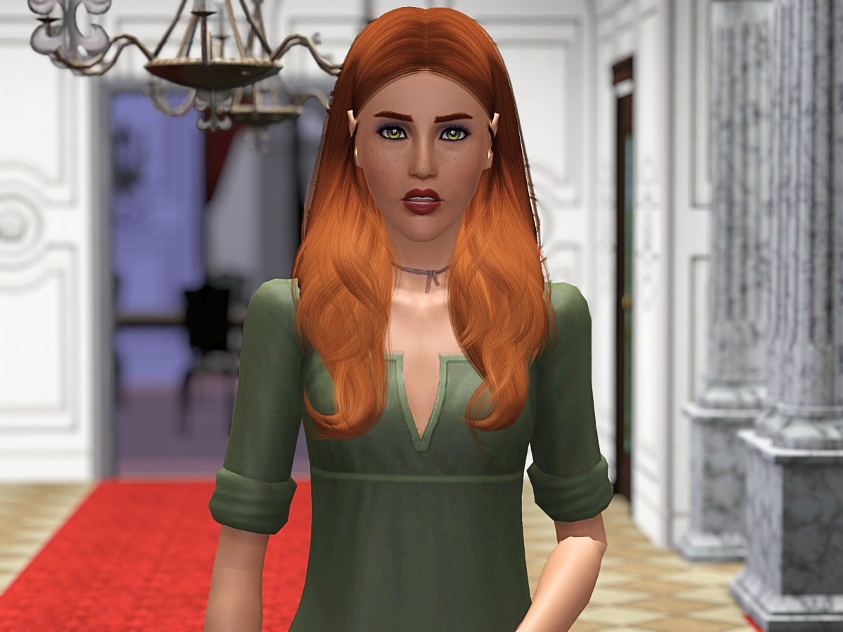 A young woman with long, wavy red hair and green eyes is standing in a corridor with a red carpet. She is wearing a green dress with rolled-up sleeves and has a neutral expression. Decorative columns and a chandelier are visible in the background.