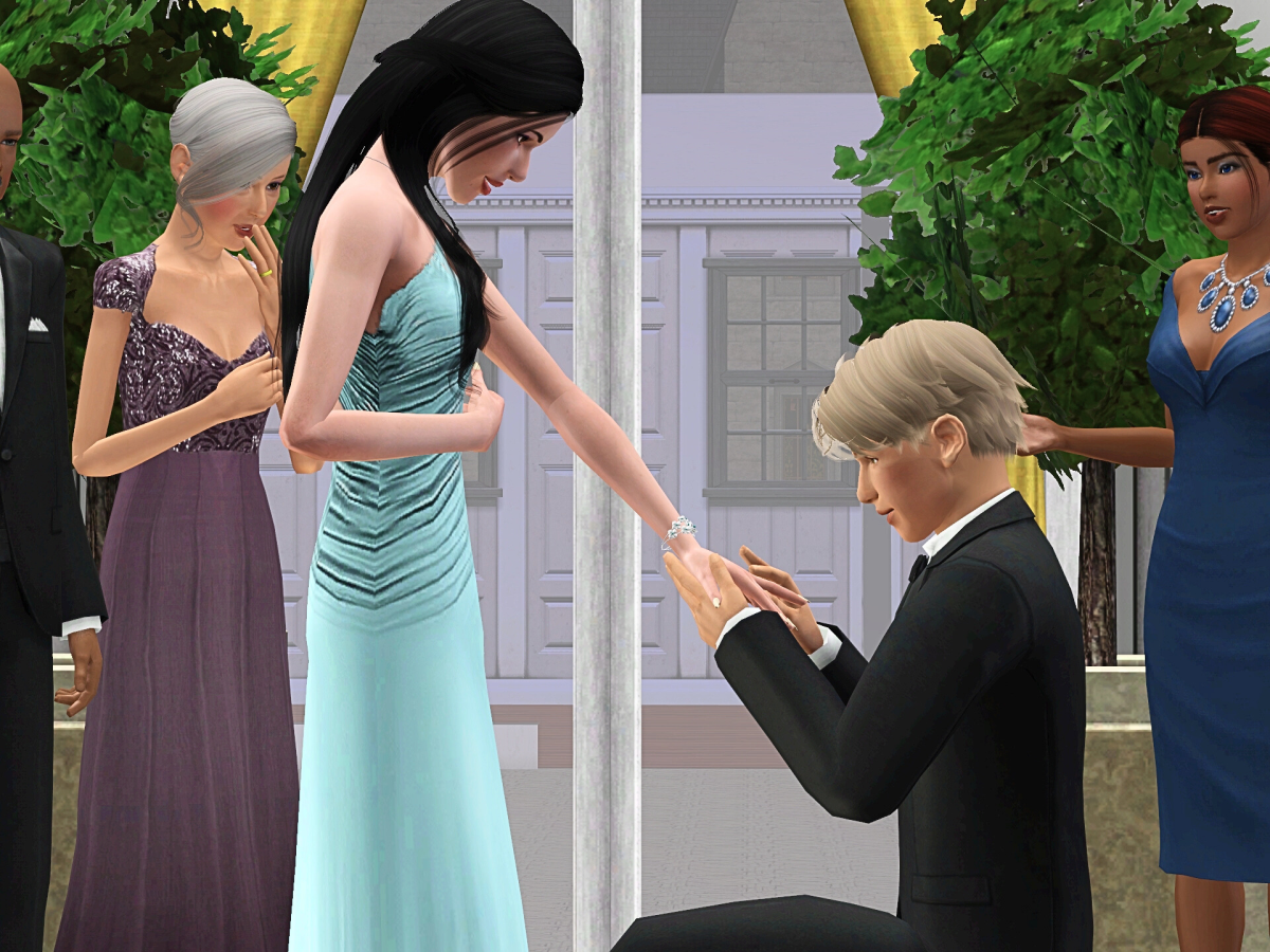 A man kneels, holding a woman's hand as he proposes. The woman, dressed in a light blue gown, looks excited. Others in formal attire watch the moment with anticipation.