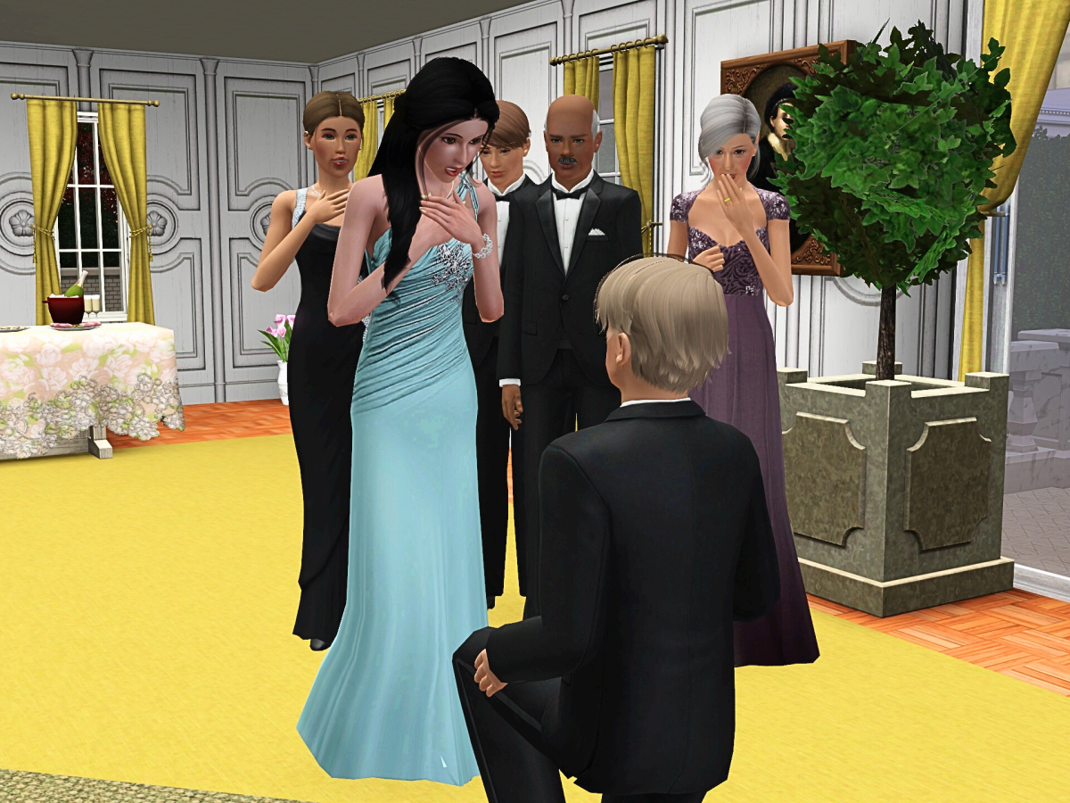 A man in a tuxedo is kneeling in front of a woman in a blue gown, surrounded by four other elegantly dressed individuals in a warmly lit room decorated for a celebration.