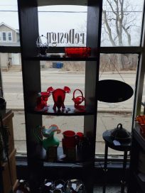 A display shelf featuring various glass items, including red glass elephant figures, vases, and other decorative pieces, seen through a window.