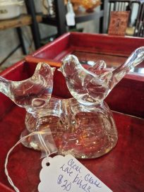 A pair of figurine birds made of clear glass, sitting closely together on a small base, with a price tag attached indicating $20.