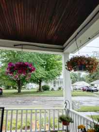A view from a porch showing hanging flower baskets, green trees, and a rainy street scene.