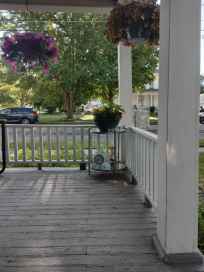 View of a porch with hanging flower baskets, a potted plant on a small table, and a suburban street in the background.