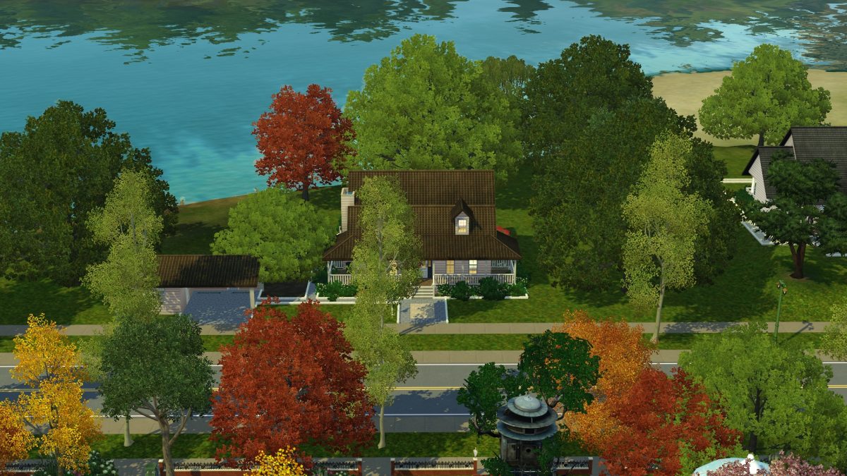 Aerial view of a house surrounded by vibrant trees in various autumn colors, with a lake in the background and a road in front.