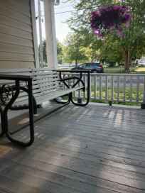 A wooden porch with a black metal bench and a hanging flower basket, surrounded by greenery.