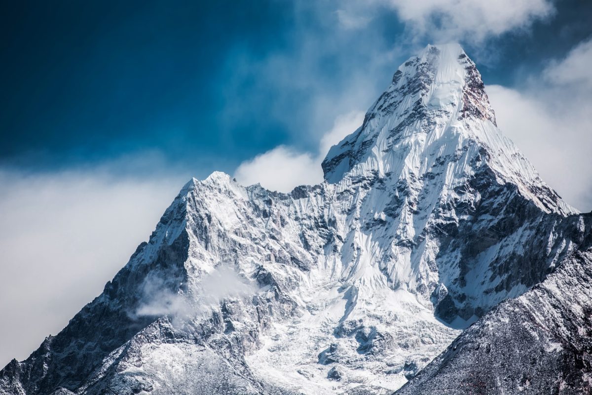Majestic snow-capped mountain peak against a clear blue sky with wispy clouds.